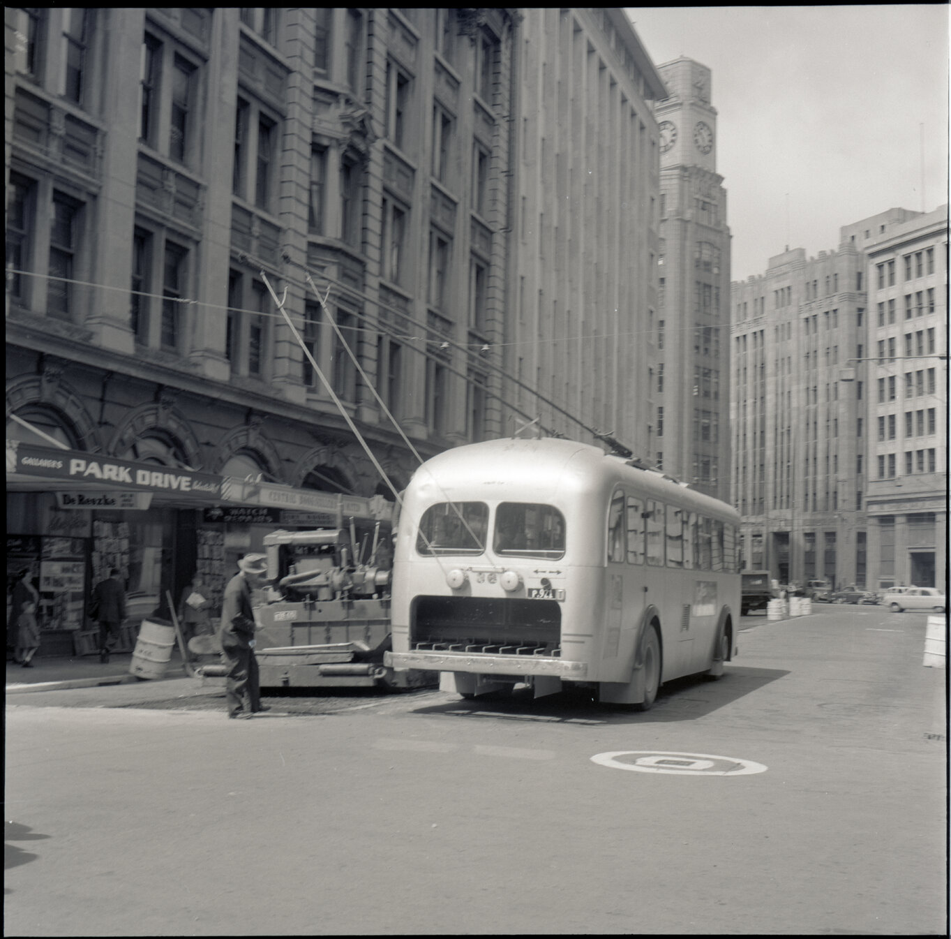 a. Various stages of asphaltic road surfacing by Council workmen, Lambton Quay end of Featherston Street. People passing by have stopped to watch work in progress. Trolly buses in background