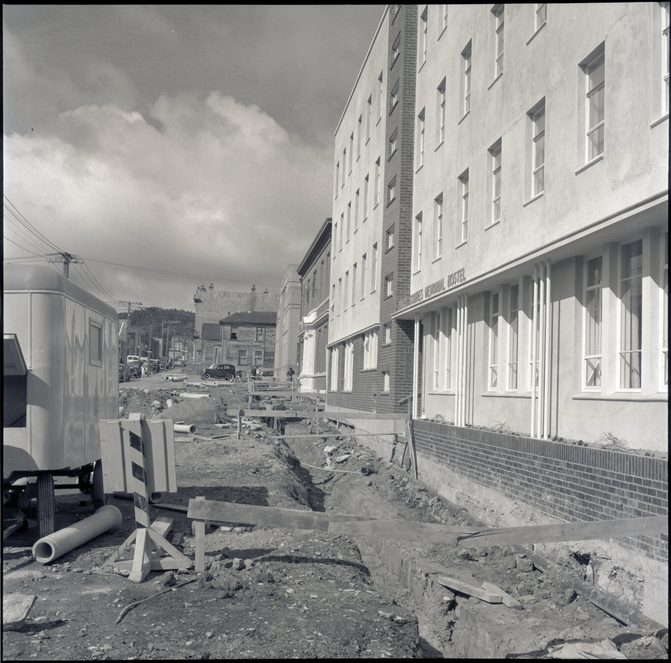 b. Various stages of asphaltic road surfacing by Council workmen, Lambton Quay end of Featherston Street. People passing by have stopped to watch work in progress. Trolly buses in background