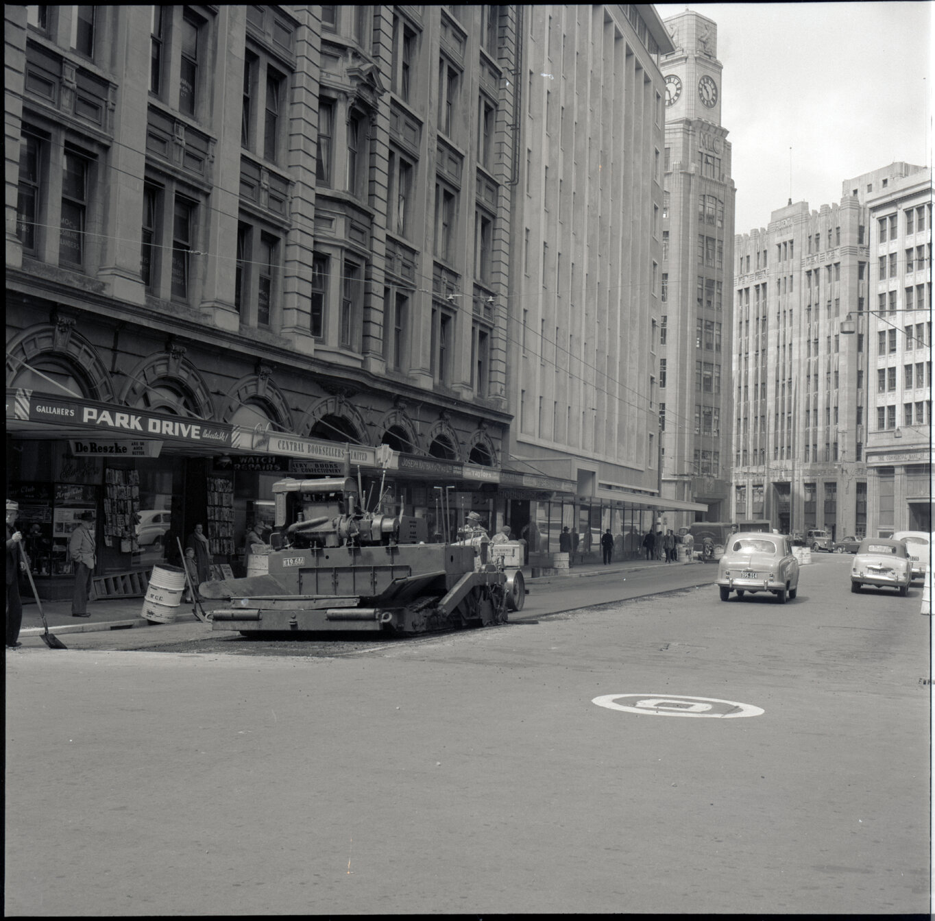 c. Various stages of asphaltic road surfacing by Council workmen, Lambton Quay end of Featherston Street. People passing by have stopped to watch work in progress. Trolly buses in background