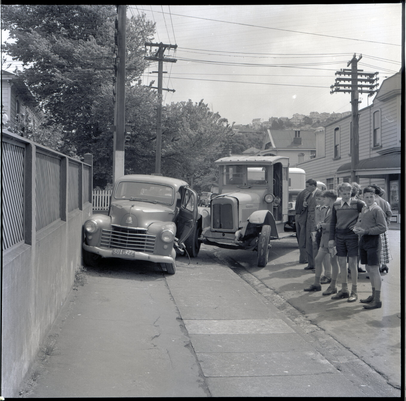 b. A flatbed truck and motor vehicle have collided, at the corner of Willis Street and Abel Smith Street. People, including men in suits and a group of young boys, have gathered. 319 Willis Street, a two storey wooden building is in the background. Gilby'