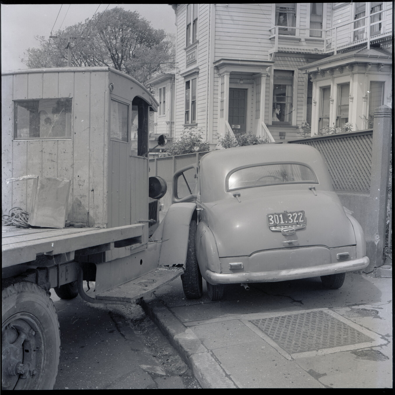 c. A flatbed truck and motor vehicle have collided, at the corner of Willis Street and Abel Smith Street. People, including men in suits and a group of young boys, have gathered. 319 Willis Street, a two storey wooden building is in the background. Gilby'