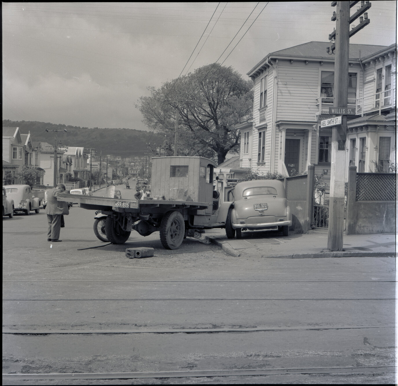 e. A flatbed truck and motor vehicle have collided, at the corner of Willis Street and Abel Smith Street. People, including men in suits and a group of young boys, have gathered. 319 Willis Street, a two storey wooden building is in the background. Gilby'