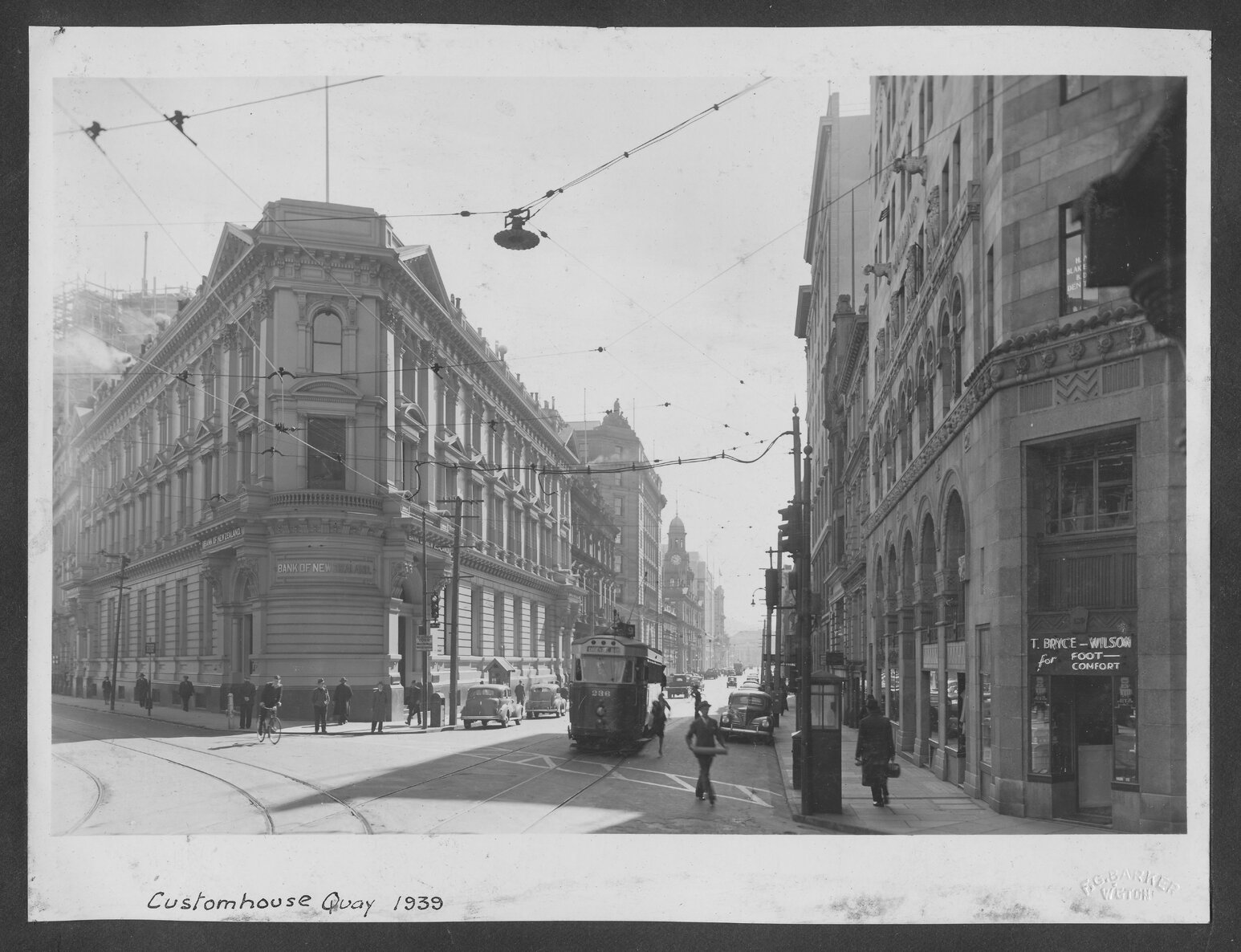 The old Bank of New Zealand building stands on the corner of Customhouse Quay and Lambton Quay. A tram is about to enter the intersection. Motor vehicles in the background. 