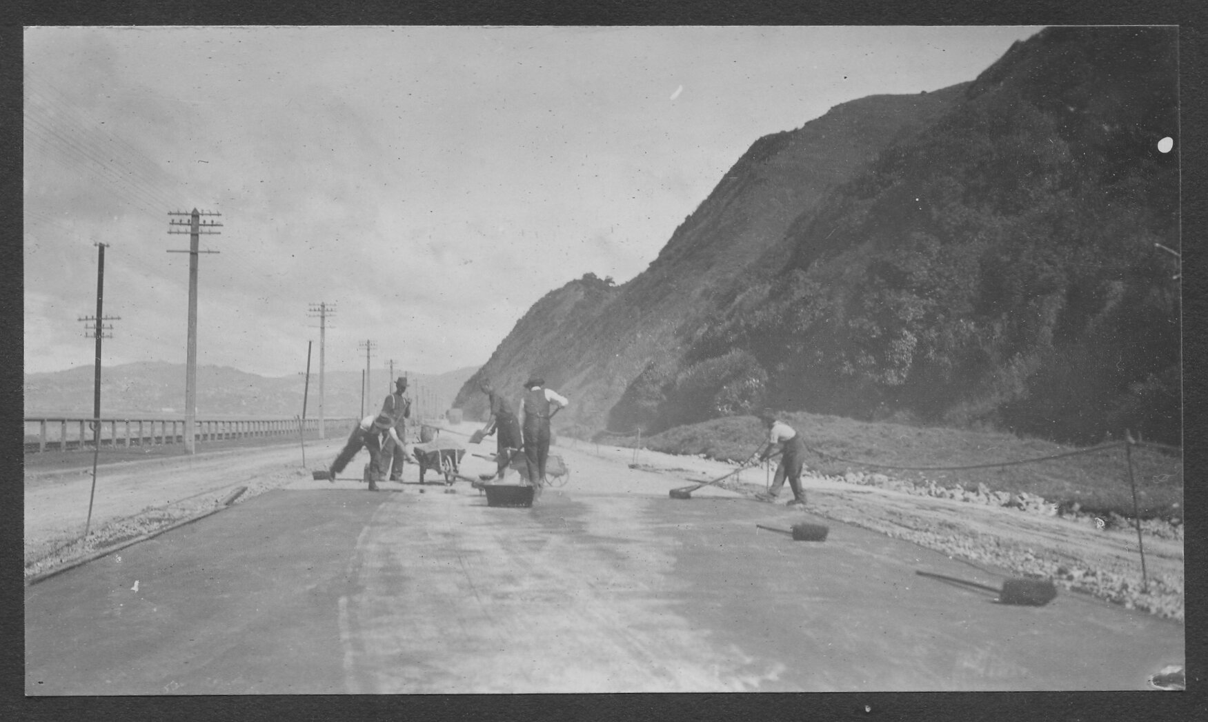 Workmen are laying new road seal on Hutt Road, motor vehicles in background.