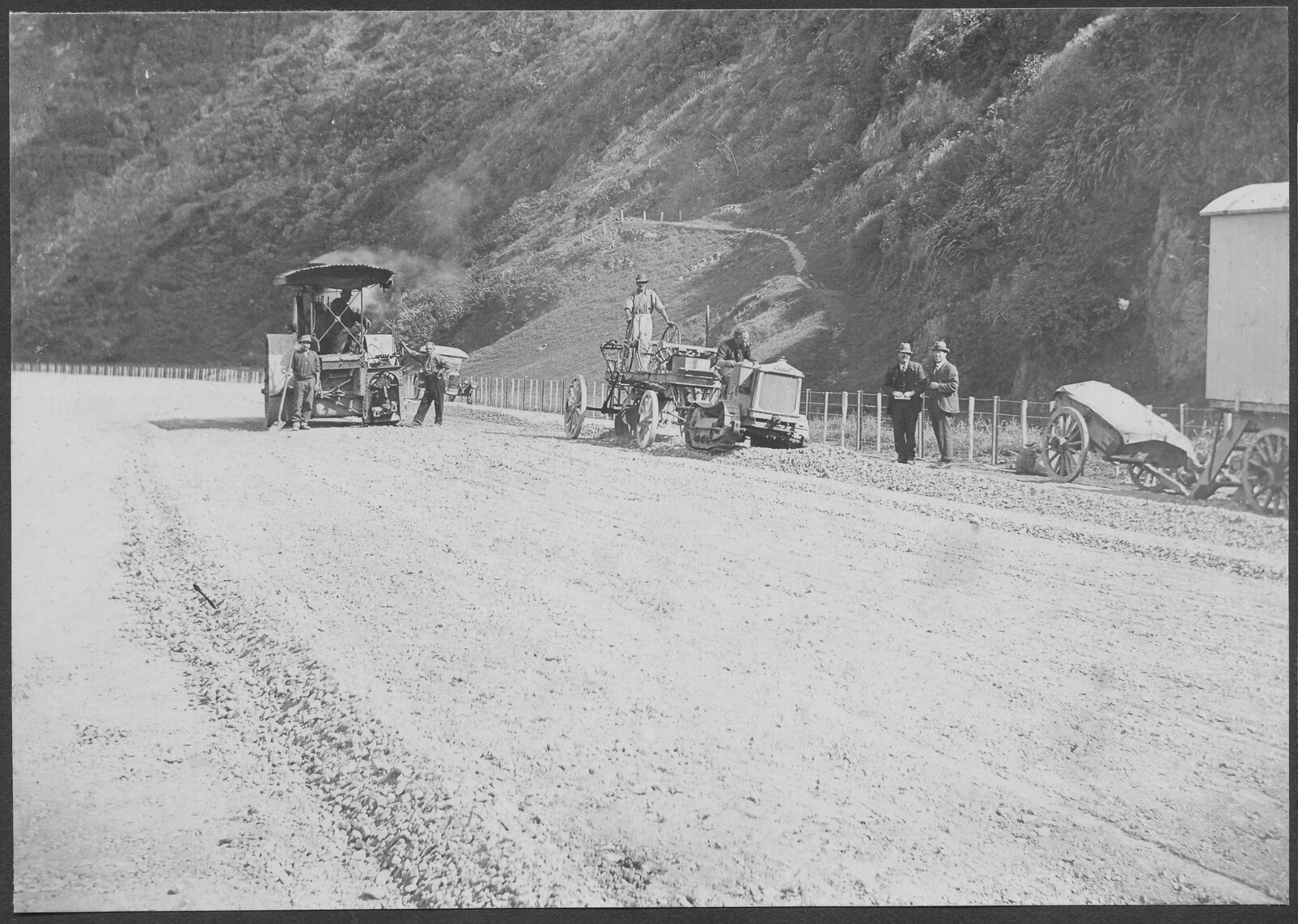 Road surface is being prepared for resurfacing, steam roller is in the background.