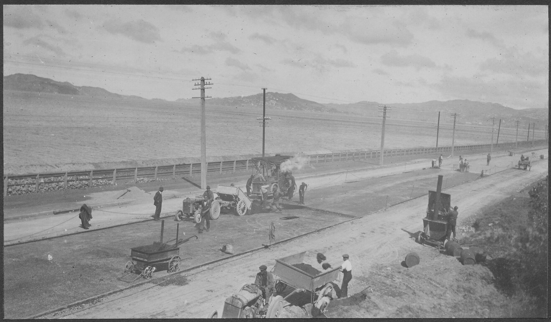 Road surface is being prepared for resurfacing, steam roller is in the background.