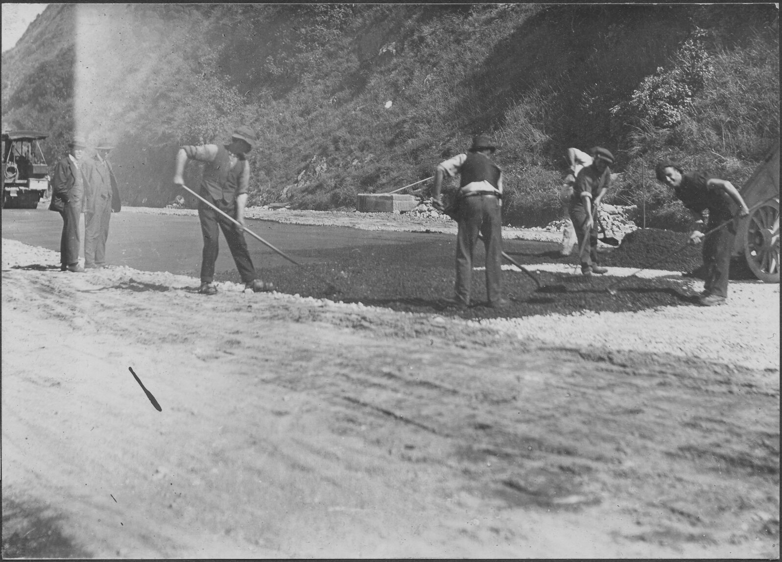 Workmen are spreading new asphalt in process of road sealing.