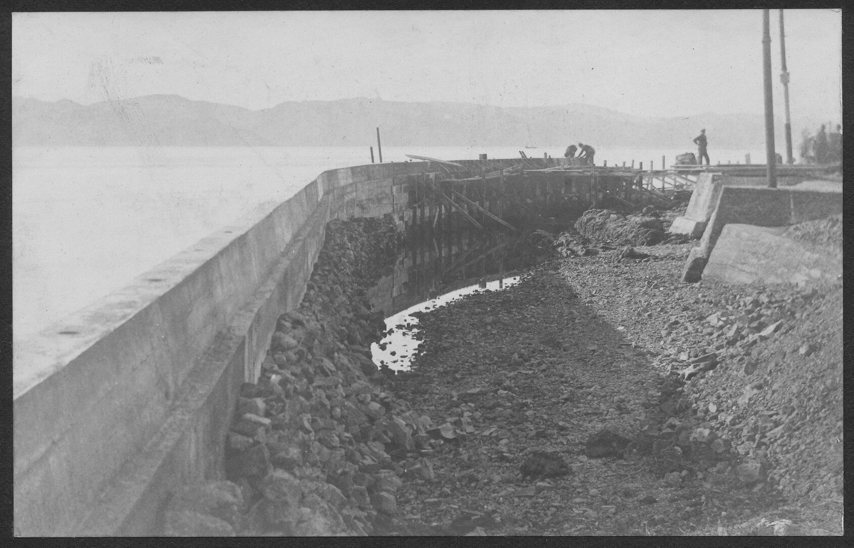Construction of seawall, workmen in background.