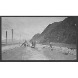 Workmen are laying new road seal on Hutt Road, motor vehicles in background.