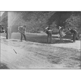 Workmen are spreading new asphalt in process of road sealing.