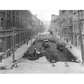 Elevated view of Victoria Street with asphaltic concrete paving in progress, number of workmen and equipment, Victoria Street