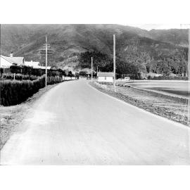 Photograph of the new alsphaltic concrete surface on Muratai Road, previously identified as Days Bay Road. Shows shoreline and a boatshed, Days Bay Beach, May 1926
