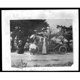 Two women wait while a man repairs the wheel on a motor vehicle