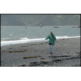 Woman on Seatoun beach with Steeple Rock Lighthouse in background